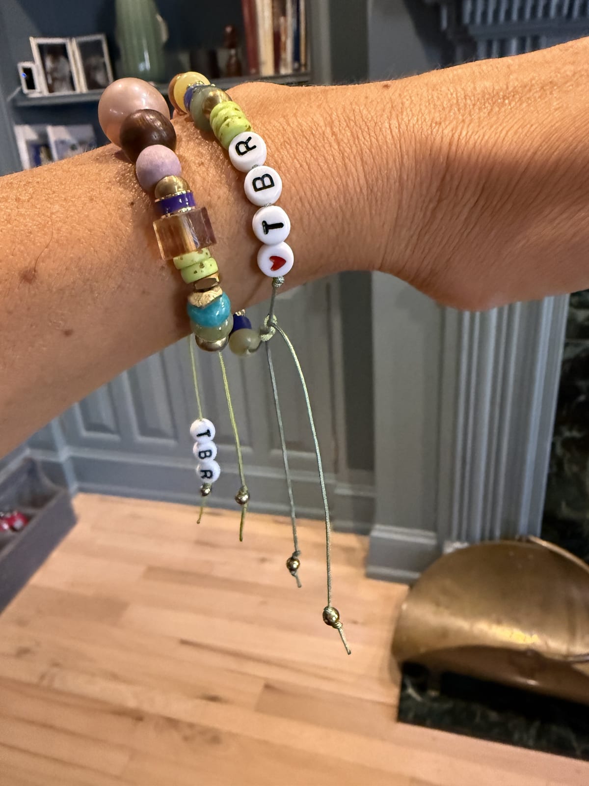 Two beaded bracelets on a wrist, one spelling TBR with a red heart and a TBR charm hanging from the cord