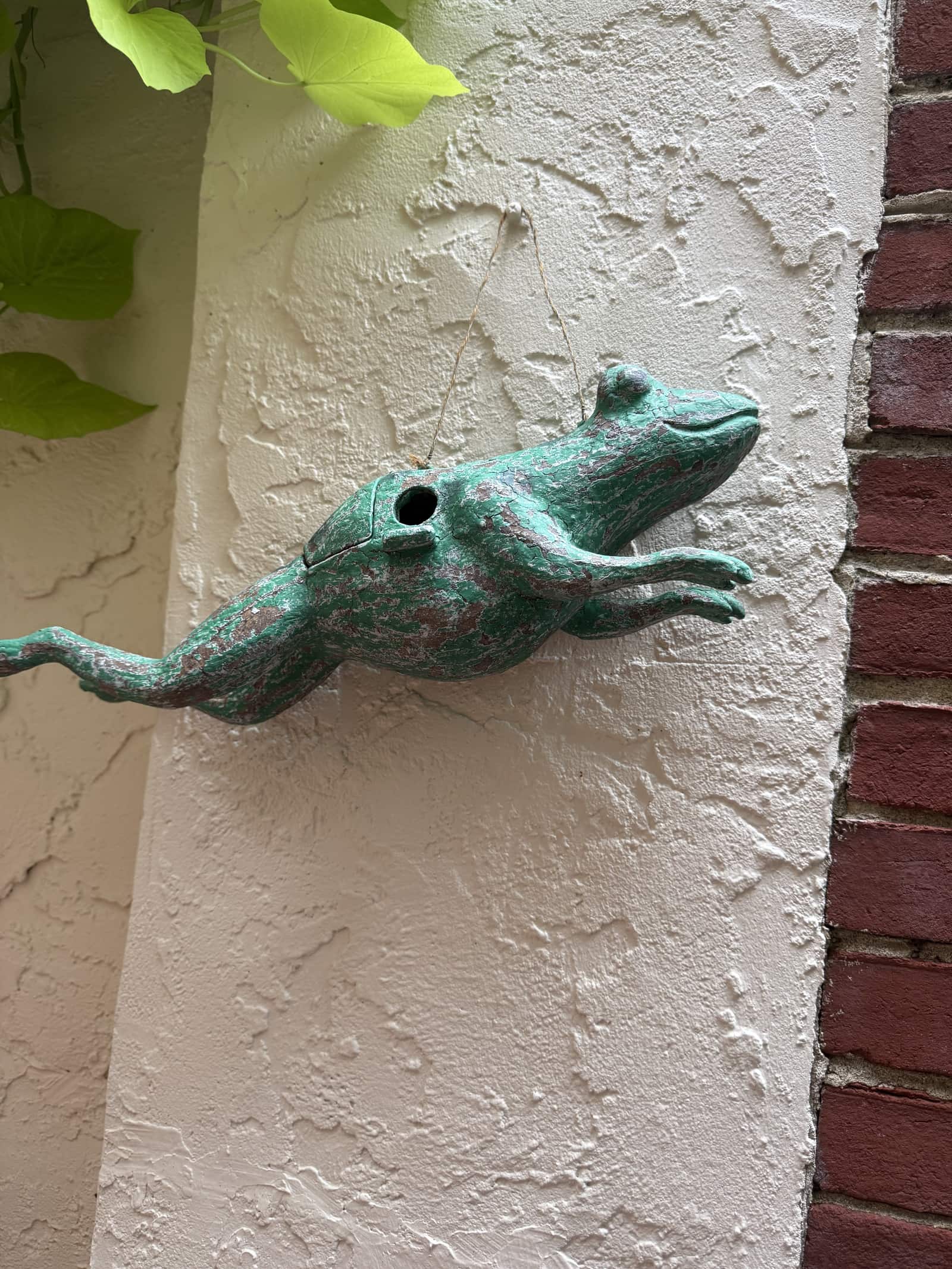 A verdigris frog-shaped spout mounted on a pale stucco wall beside red brick