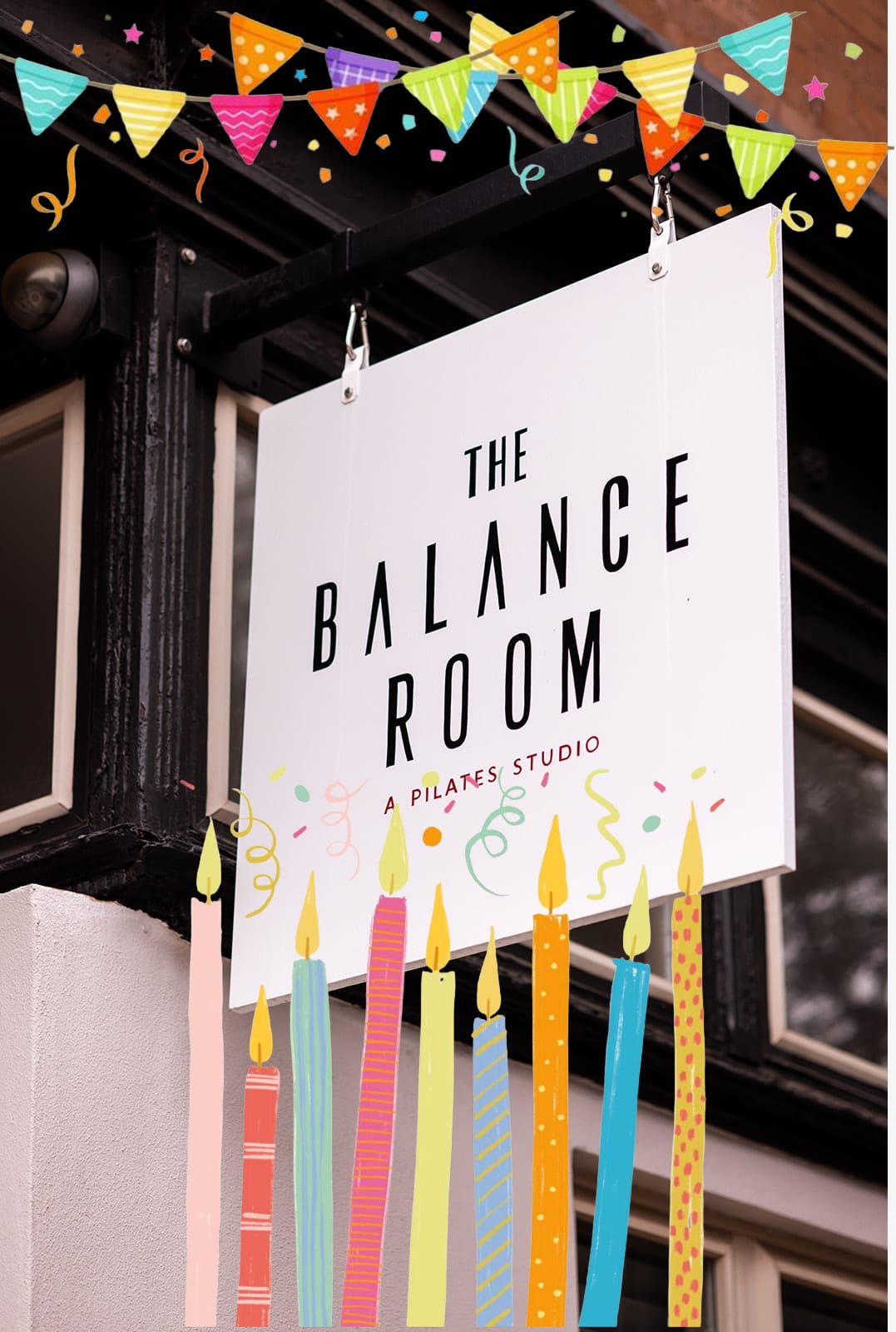 The Balance Room’s hanging street sign under drawn bunting, with birthday candles across the bottom